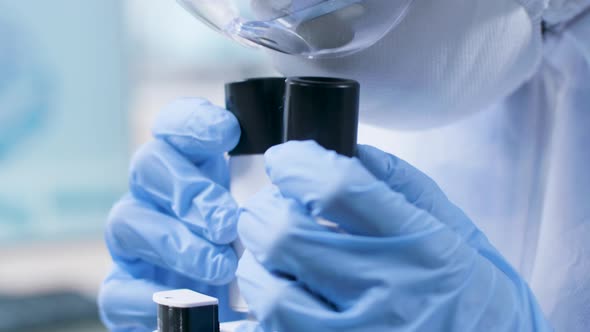 Handheld Close Up Shot of Professional Scientist in Coverall Looking Into the Microscope