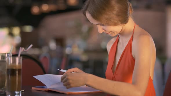 Girl Reads Diary Sitting at Table Near Beverages