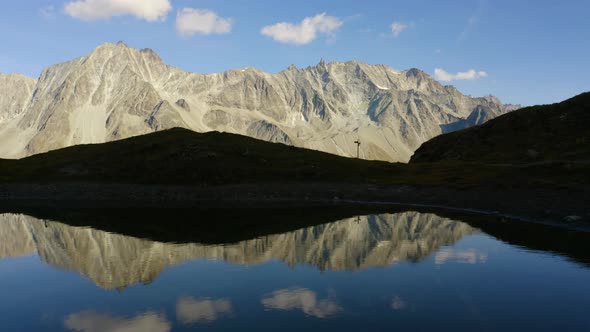 Flying low and sideways above perfect mirror lake with high mountain peak in the backgroundAutumn c