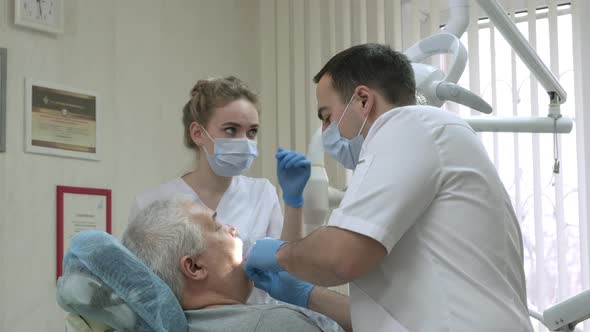 Dentist with Nurse in Protective Masks Working with Patient in Dental Clinic