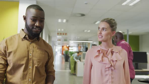 Diverse male and female business colleagues talking and walking in office