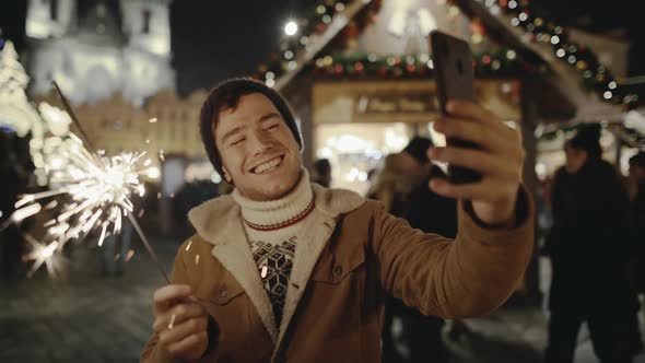 Funny Young Guy Smiling and Making Selfie with His Smartphone at Amazing Street Fair in Old European