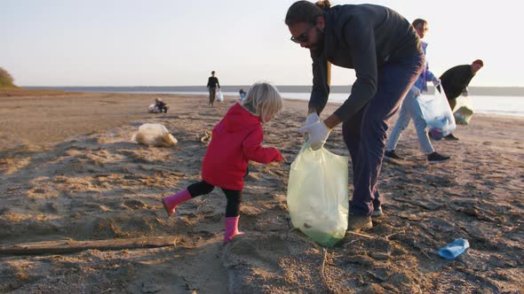 Little Girl Helps Her Parents to Clean Up Area of Dirty Beach with Garbage Bags Slow Motion