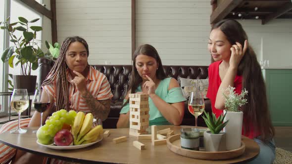 Mixed Race Female Friends Playing Wooden Board Game Sitting Indoors