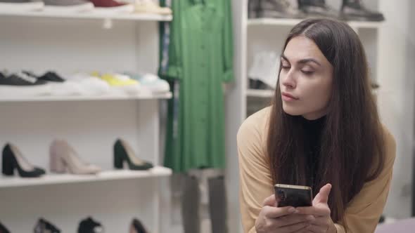 Shoe Shop with Gorgeous Young Caucasian Woman Waiting for Order Sitting on the Right Scrolling