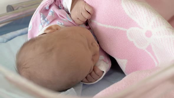 A closeup of a newborn baby sleeping under the pink blanket