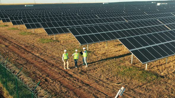 Top View of Three Solar Panel Technicians Examining a Solar Farm