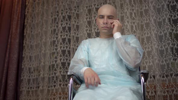 A Bald Young Man with Oncology Looks Sadly at the Camera. The Patient Adjusts the Breathing