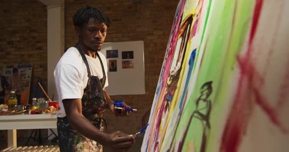 African american male artist wearing apron painting with palette knife on canvas at art studio