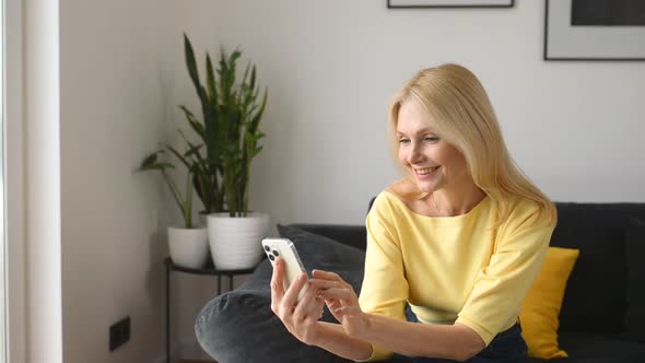 Smiling Middleaged Woman with a Smartphone Sitting on the Sofa at Home