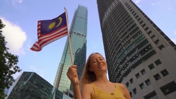 Slow Motion Shot of a Young Woman That Waves Malaysian Flag with Skyscrapers at a Background