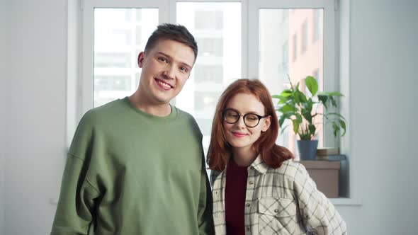 Young Man and Woman Looking at Camera in Empty Apartment and Smiling