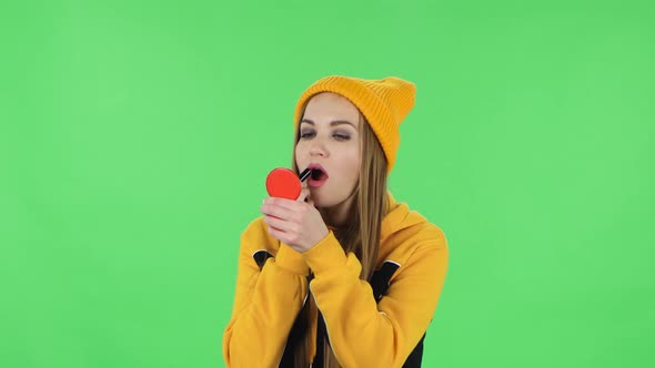 Portrait of Modern Girl in Yellow Hat Is Painting Her Lips Looking in Red Mirror. Green Screen