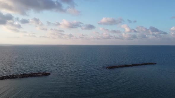 Aerial mesmerizing shot of wave blockers in the sea, light clouds and clear horizon