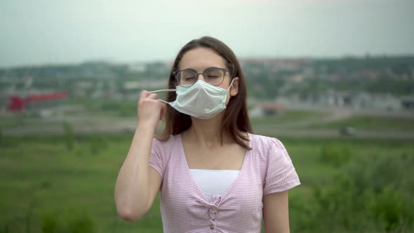 A Young Woman with Glasses Takes Off Her Medical Mask and Breathes Freely