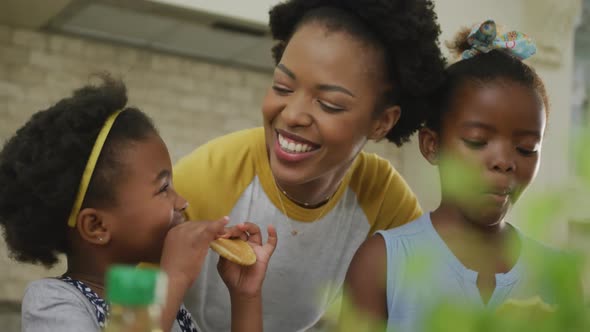 Happy african american mother with daughters eating in kitchen