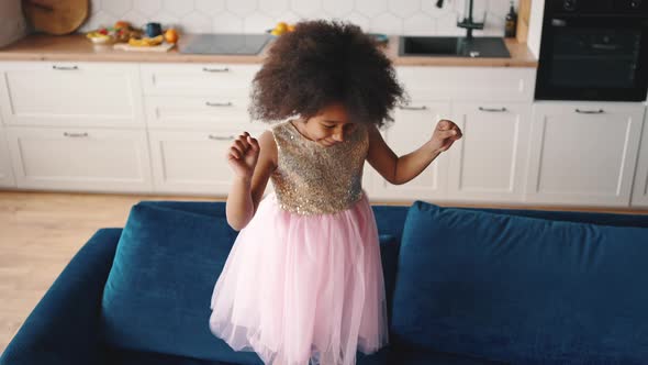 Top View of Cheerful Little African American Girl Having Fun at Home Jumping on Blue Sofa and