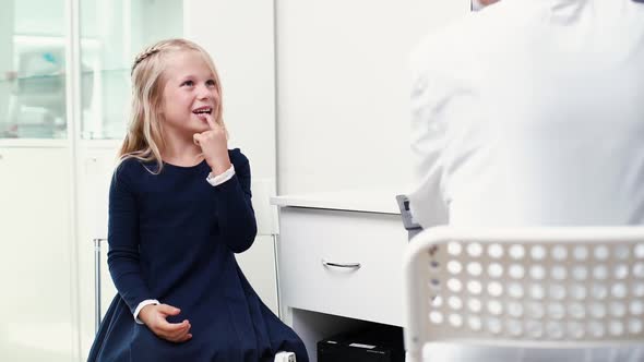 Cute Funny Blonde Kid Girl Patient Sit on Chair Talking To Woman Doctor