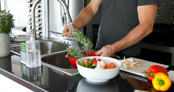 Man washing vegetable under water tap in kitchen 