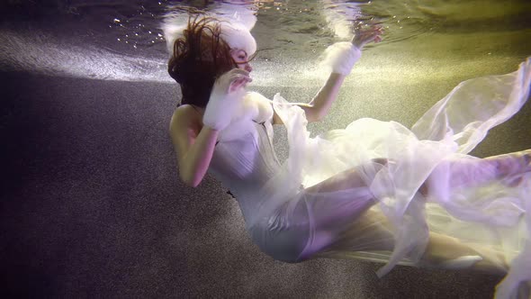 Pretty Girl Dressed Like Winter Fairy Is Floating in Water of Pool, Subaquatic Shot