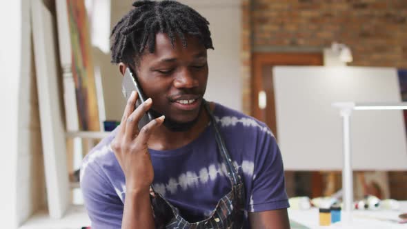 Smiling african american male painter talking on smartphone in artist studio