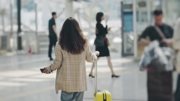 View From Back of Businesswoman Moving Along Airport Terminal with Smartphone in Hand