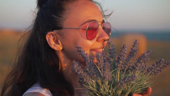 Closeup Side View Portrait of Beautiful Young Woman in Sunglasses Enjoying Fragrance of Flowers