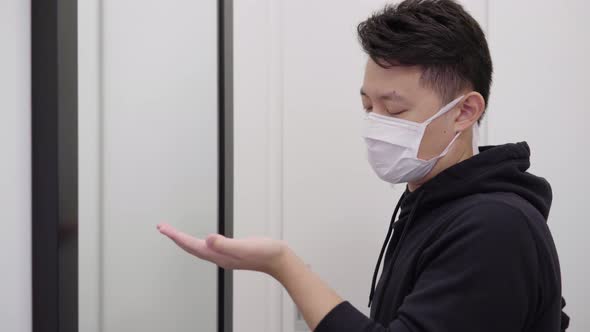 A Young Asian Man in a Face Mask Applies Disinfection Gel on His Hands and Looks in a Mirror