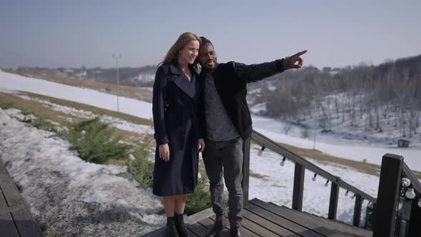 Smiling African American Loving Man Pointing Away Talking with Caucasian Woman Standing on Hotel