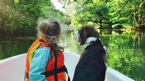 Girl child and her pet beagle dog are floating down a river on a boat and looking ahead.