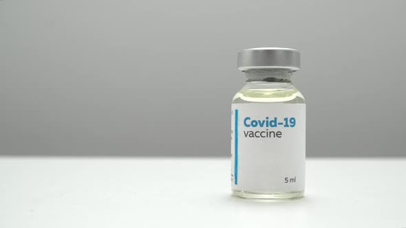 Close up panning of a COVID-19 vaccine bottle on a white clinic table.