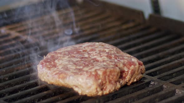 Slow motion of beef hamburger on a grill in close up with flames and smoke