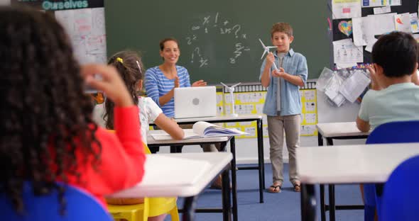 Front view of Caucasian schoolboy explaining about windmill model in the classroom 4k