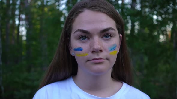 Headshot of Young Brunette Ukrainian Woman with Blue and Yellow Strips Painted on Face Looking at