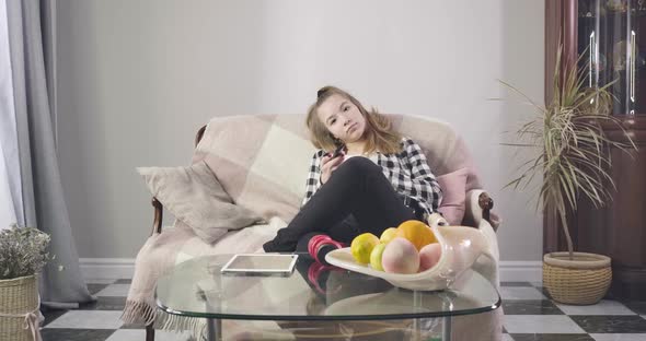 Portrait of Teen Caucasian Girl Sitting on Couch and Watching TV. Pretty Young Lady Watching Movies