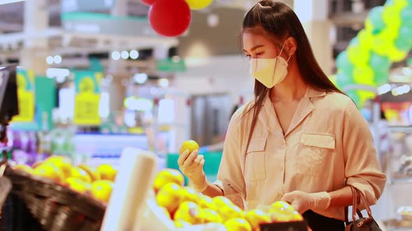 Beautiful attractive asian woman wearing medical face mask and rubber gloves choosing orange