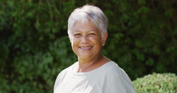 Video of happy biracial senior woman looking at camera in garden