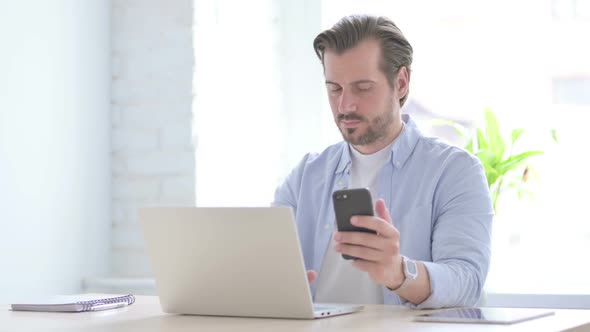 Young Man Using Smartphone While Using Laptop