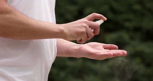 Man disinfecting his hands with sanitizer outdoors in city.