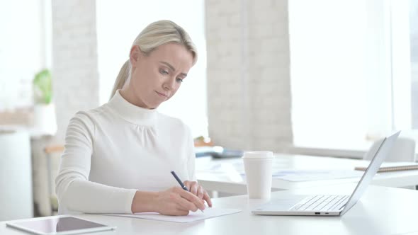 Upset Young Businesswoman Writing Documents on Office Desk