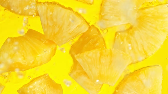 Super Slow Motion Shot of Pineapple Slices Falling Into Water on Yellow Background at 1000Fps.