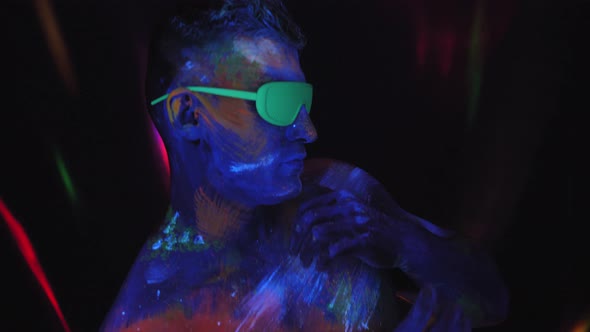 A Muscular Man with Ultraviolet Drawings on His Body Is Dancing in the Dark