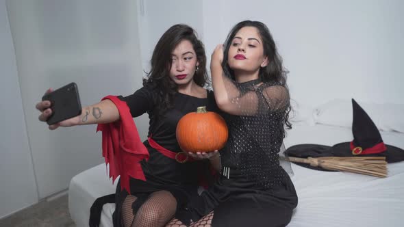 Pretty Women In Halloween Witch Costumes Taking Selfies In The Bedroom While Holding A Pumpkin