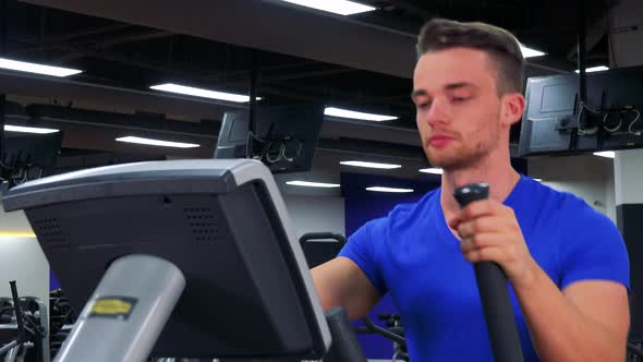 A Young Fit Man Trains on an Elliptical Trainer in a Gym - Closeup