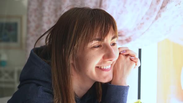 Portrait of Caucasian Young Woman Sitting in Cafe in Front of Window Looking at Camera and Smiling