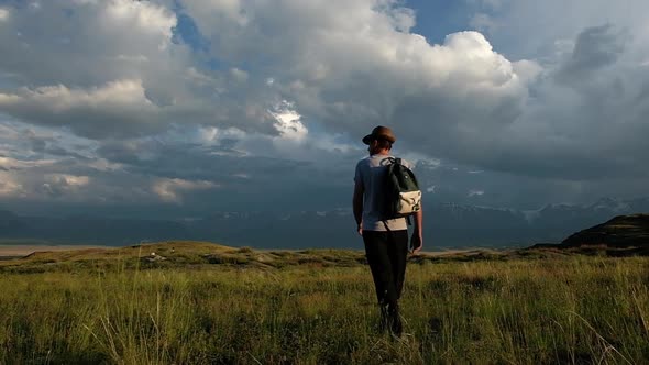 Adult tourist with a backpack walks against the background of the mountains