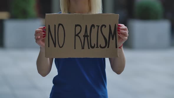 NO RACISM on a Cardboard Poster in the Hands of White Female Protester Activist. Closeup of Poster