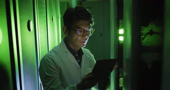 Asian male it technician in lab coat using tablet checking computer server