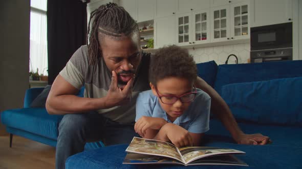 Loving Black Father and School Age Son Sharing and Discussing Comics at Home alt
