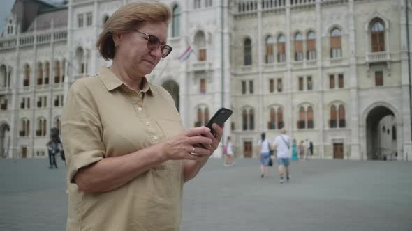 Senior Woman Using Cellphone By Parliament of Budapest Hungary